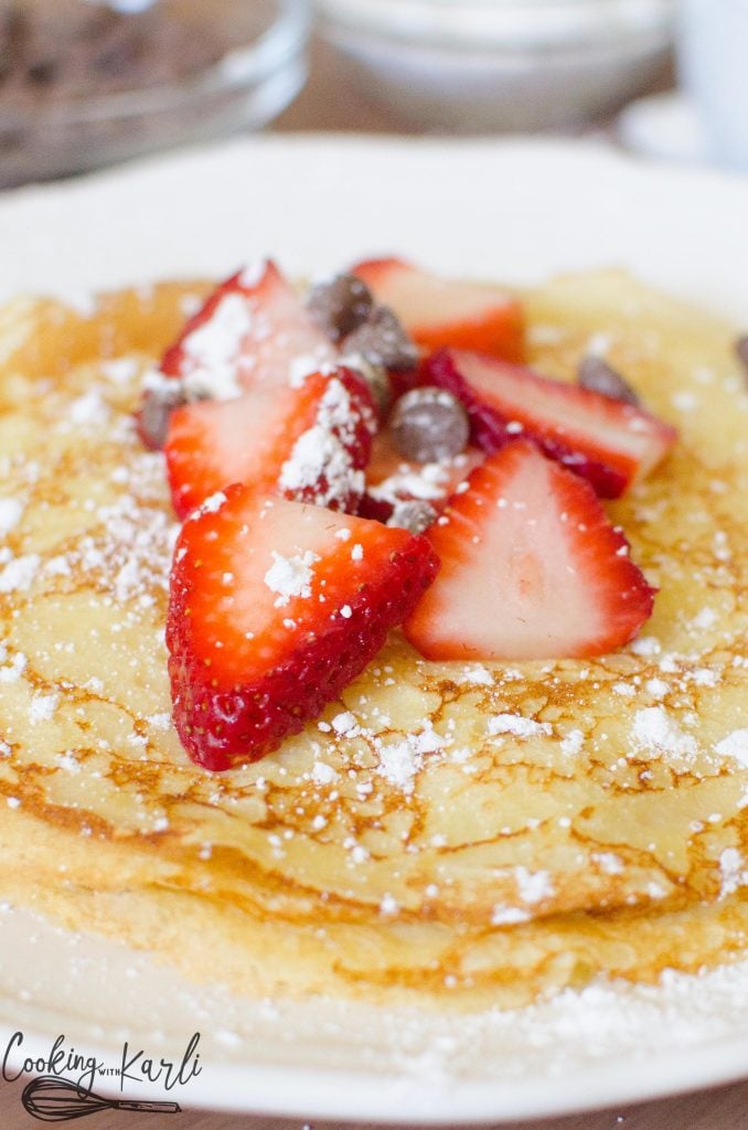 Strawberries, chocolate chips and powdered sugar piled high on a stack of crepes.