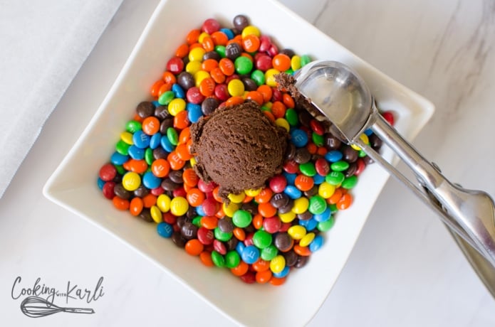 A scoop of cookie dough resting in a bowl of mini m&ms.