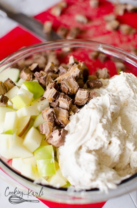 apples, candy bar and cool whip mixture big tossed together in a bowl.
