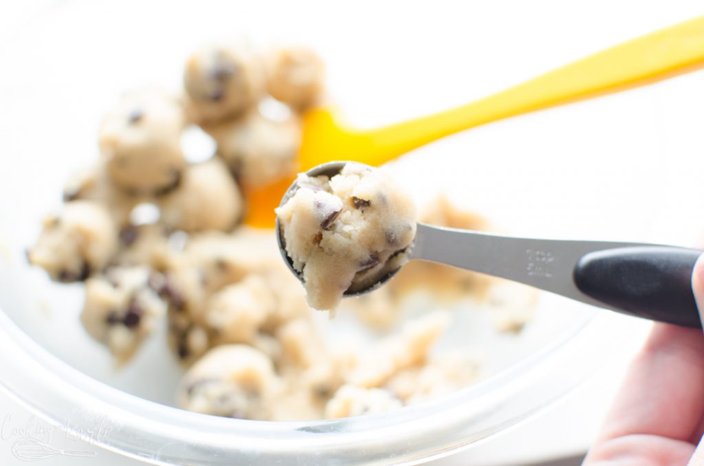 mini chocolate chip cookie dough being measured out in a tsp measuring spoon
