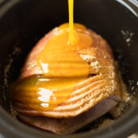 ham in the crockpot with glaze being poured on it.