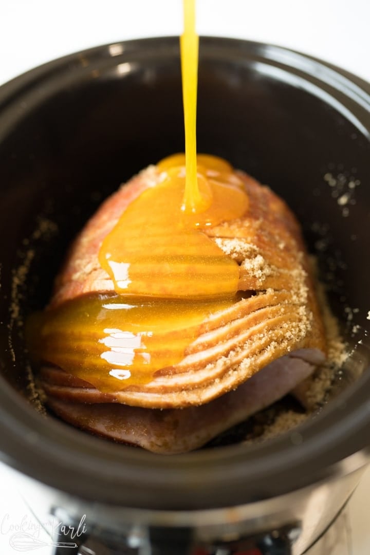 ham in the crockpot with glaze being poured on it. 