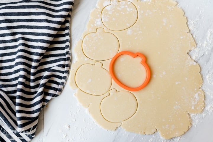 sugar cookie dough being cut with pumpkin cookie cutters for halloween