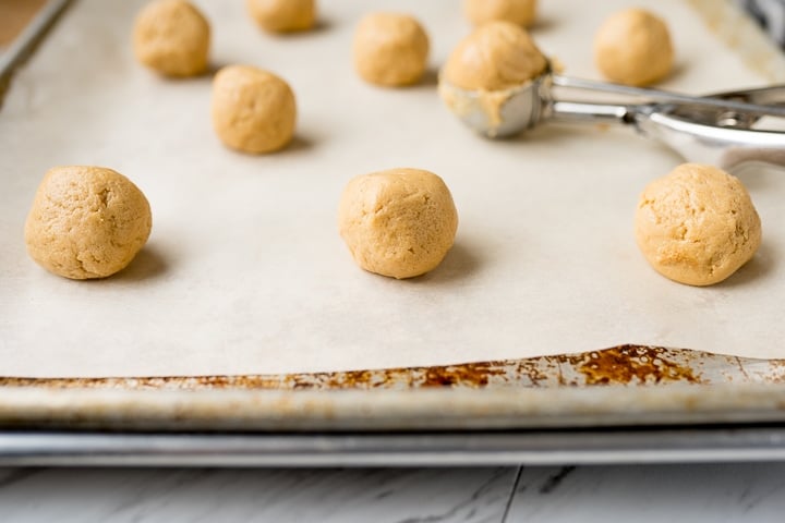 Peanut butter cookie dough scooped, rolled and placed on parchment paper.