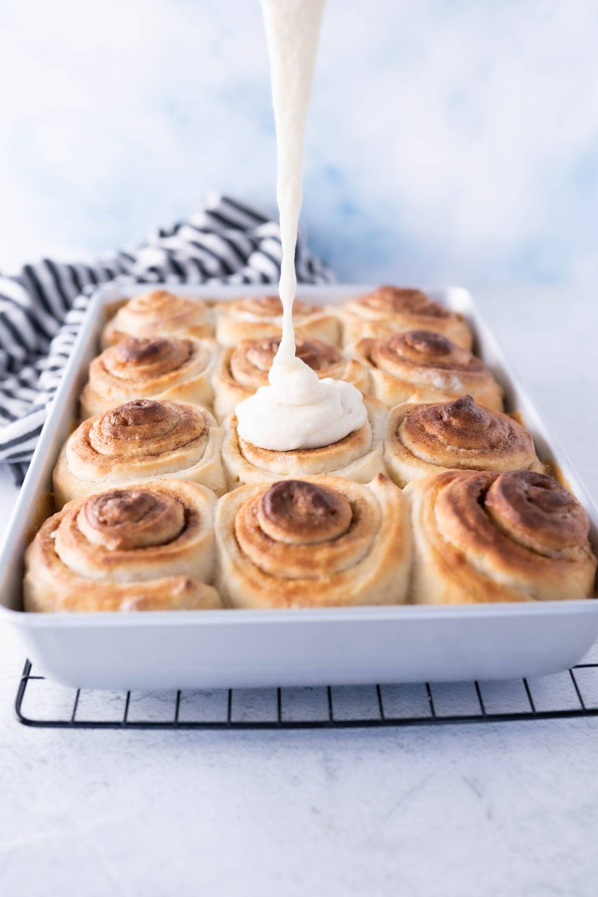 cinnamon roll icing being poured onto baked cinnamon rolls. 