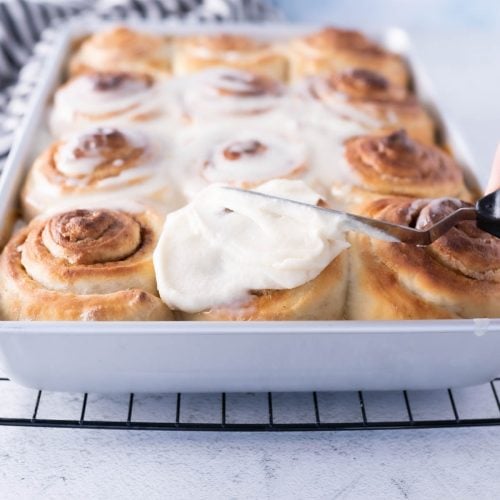 cinnamon rolls with cinnamon roll icing being spread onto the rolls.