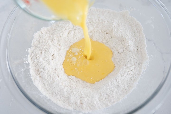 eggs being poured into a flour mixture for homemade egg noodles