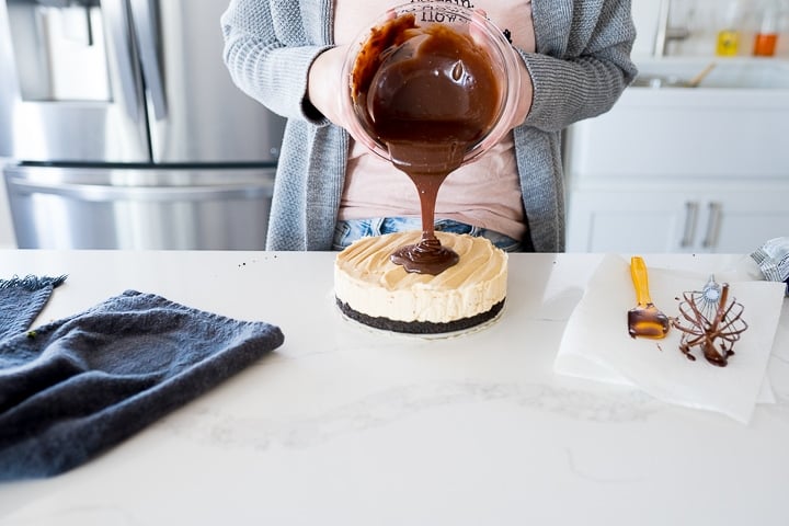 Pouring chocolate ganache onto the peanut butter cheesecake
