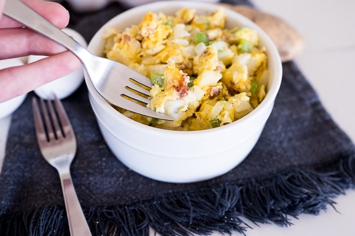 eggs, hash browns, onions, bell pepper and cheese cooked together and served in a white bowl.