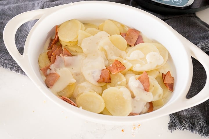 potatoes and ham being layered in the baking dish