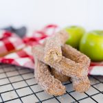 Cinnamon and sugar churros stacked on a cooling rack with apples in the background