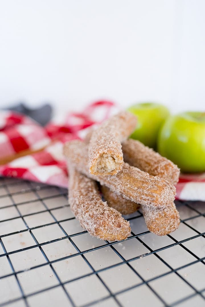 Cinnamon and sugar churros stacked on a cooling rack with apples in the background