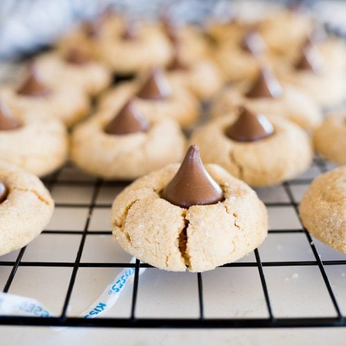 peanut butter cookies with kisses on top, one in focus on a black cooling rack