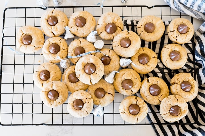 Lots of peanut butter cookies with kisses on top, on a black cooling rack