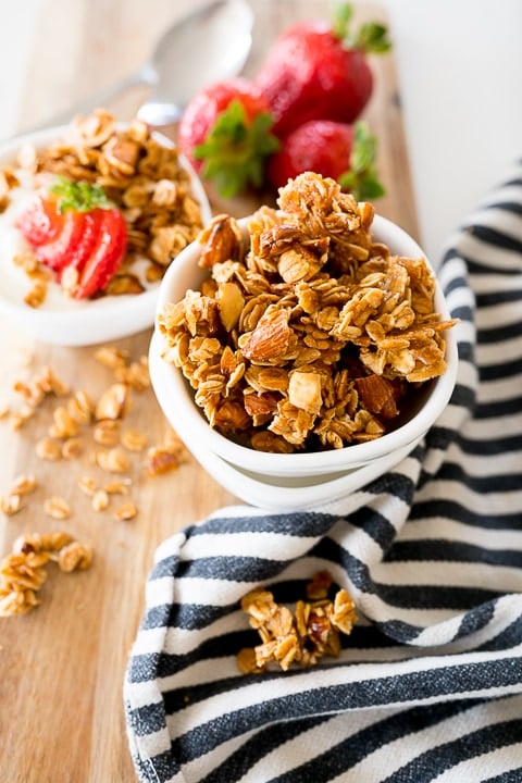 homemade granola in a white bowl with strawberries behind