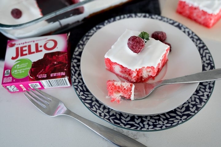raspberry poke cake with a raspberry on top and jello on the side