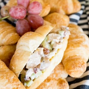 chicken salad inside of a croissant, with grapes and celery around it.