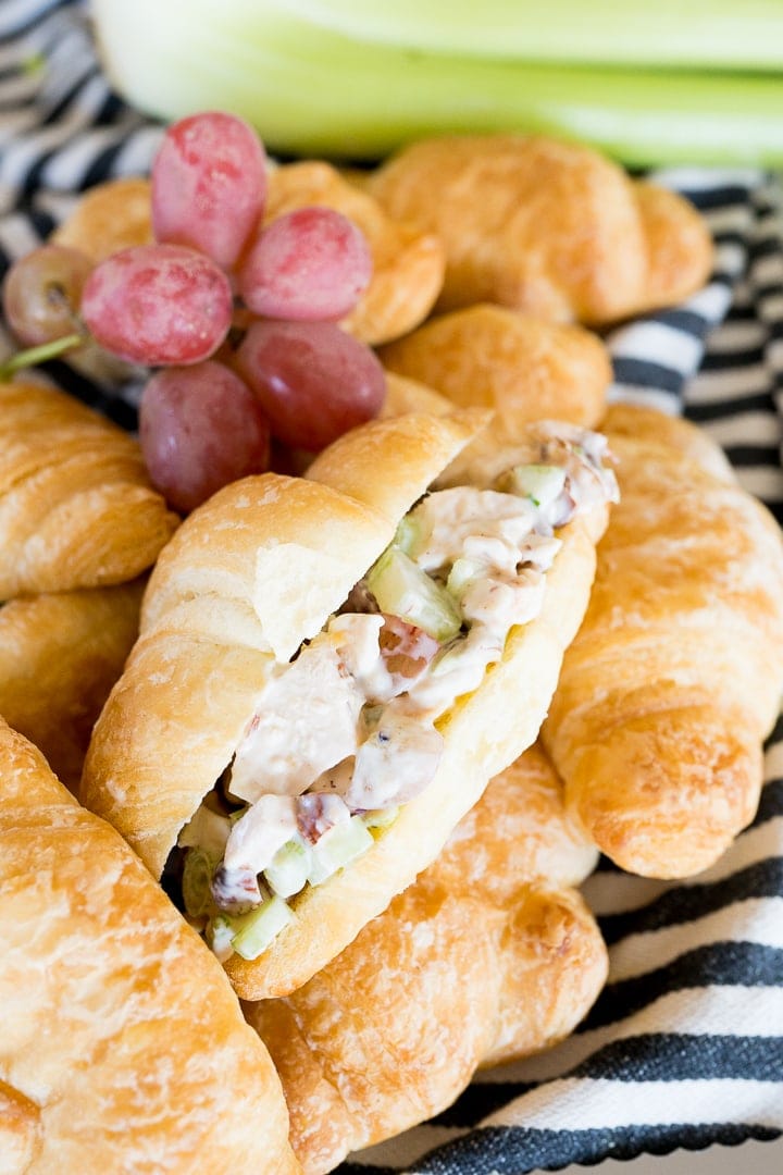 chicken salad inside of a croissant, with grapes and celery around it.