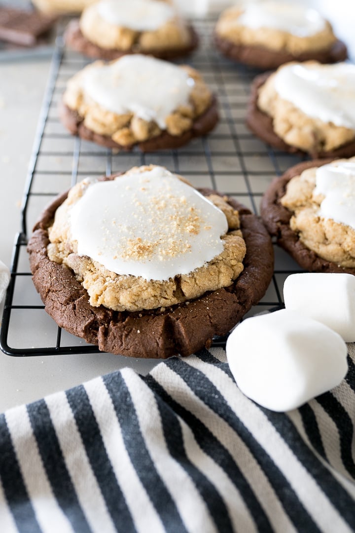 smores brownie cookies on a black cookie cooling rack with large marshmallows in the frame