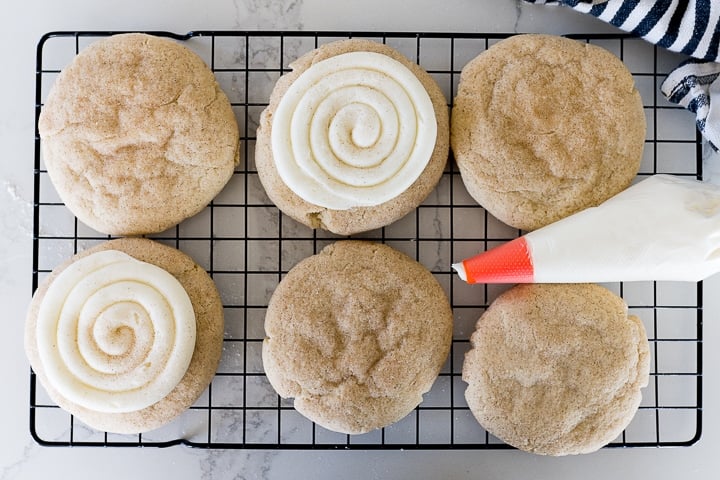 snickerdoodle cookies on a cooling rack, two of the cookies have white frosting swirled on top