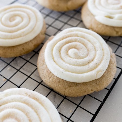 snickerdoodle cupcake cookies on a cooling rack with swirled frosting and cinnamon and sugar