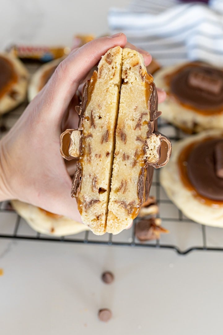 Twix cookies, cut in half, being held in the center of the frame