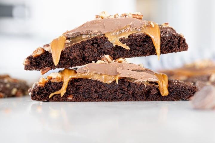 fudgey brownie cookie broken in half with caramel and milk chocolate on top.