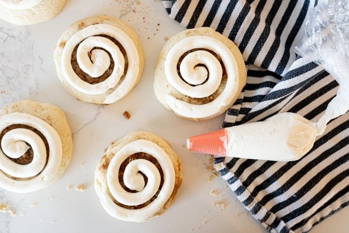 cinnamon swirl cookies on the counter with a striped towel and frosting in a piping bag. 