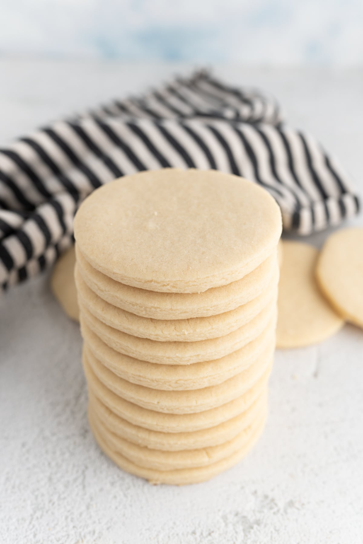 a stack of circle sugar cookies with a striped dishtowel behind it. 