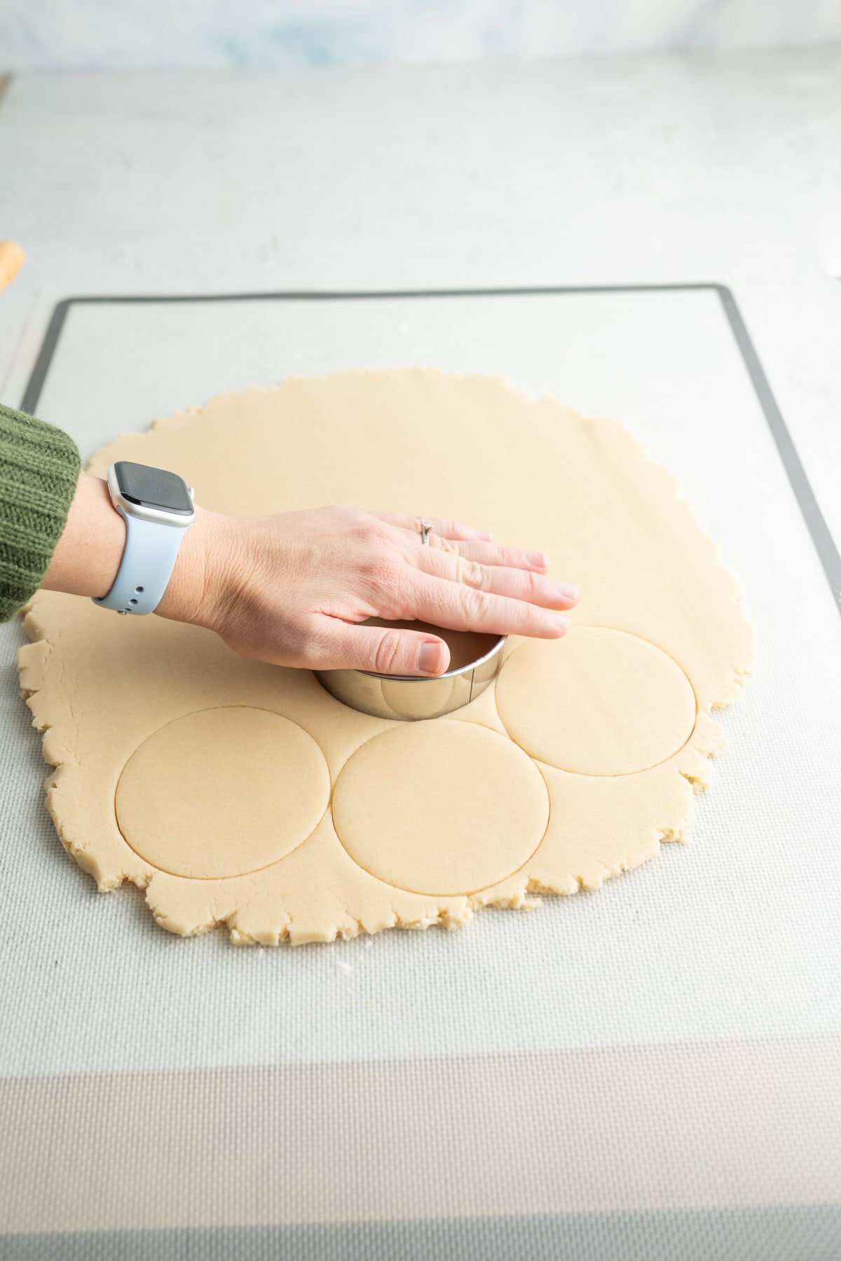 circle sugar cookies being cut out of rolled out sugar cookie dough. 