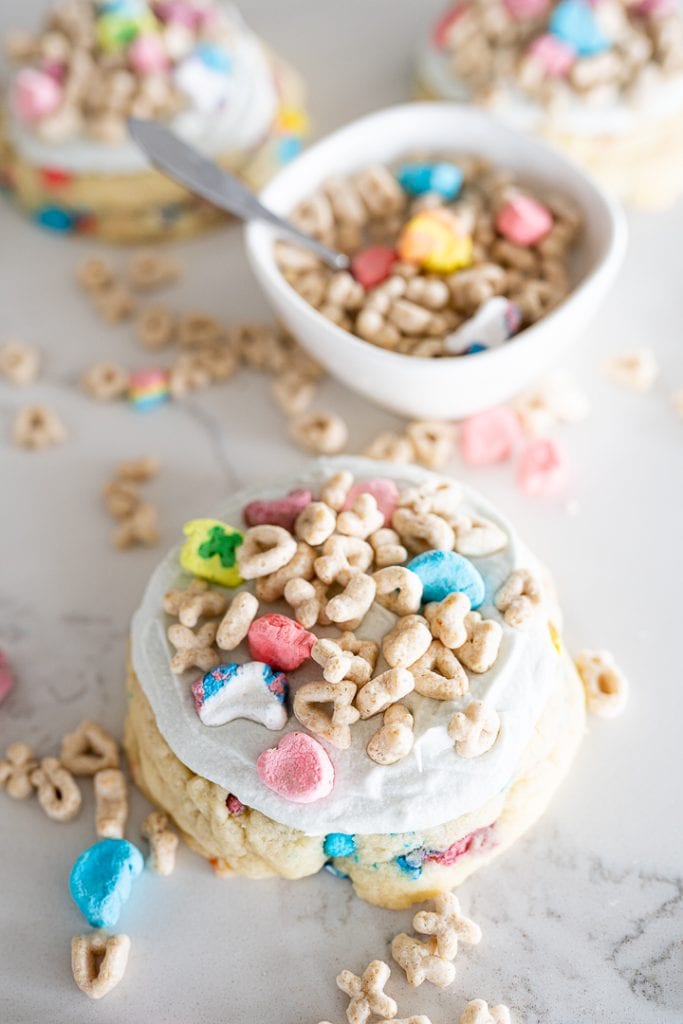 sugar cookie with cereal milk frosting on the counter with lucky charms by it