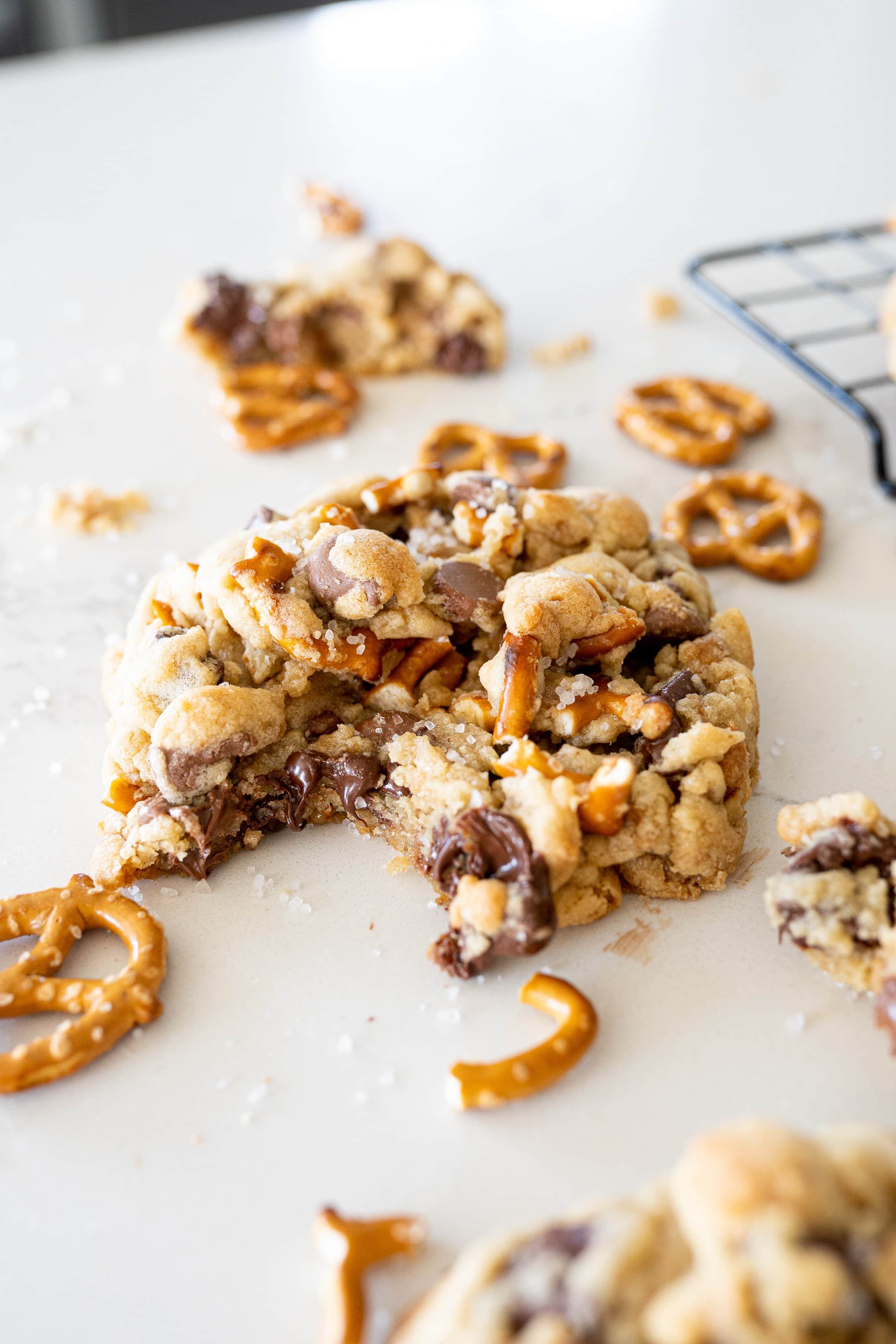 a cookie with melted chocolate chips, pretzels and toffee with sea salt on top on the counter, with a bite taken out of it.