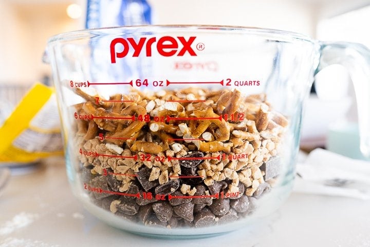 a large measuring bowl full of chocolate chips, chocolate chinks, toffee bits and pretzels.