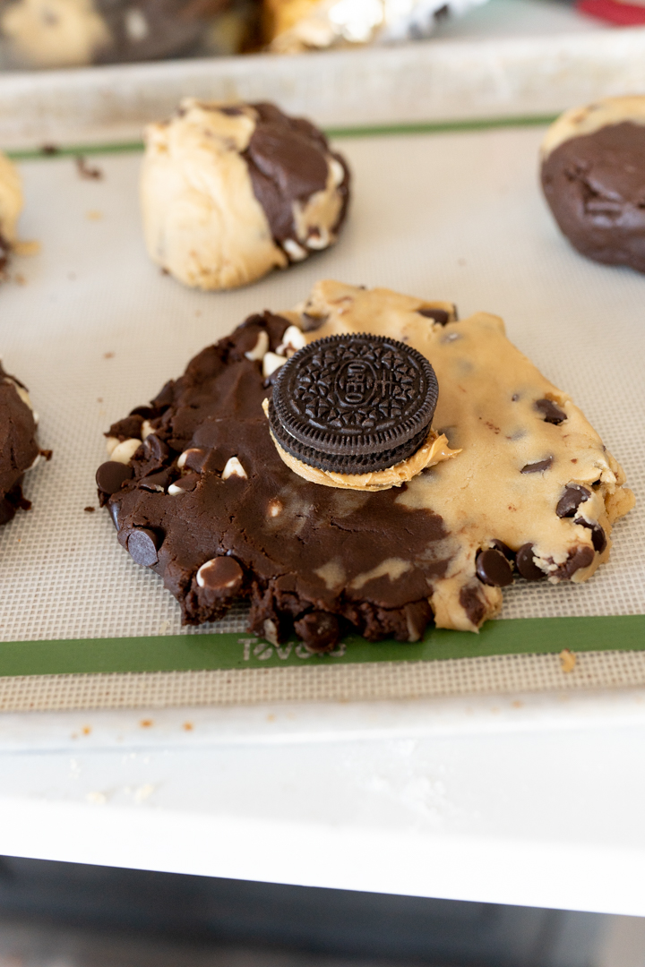 Brookie oreo cookies being made- the cookie dough is smashed flat and then a peanut butter topped oreo is placed in the center of the dough.