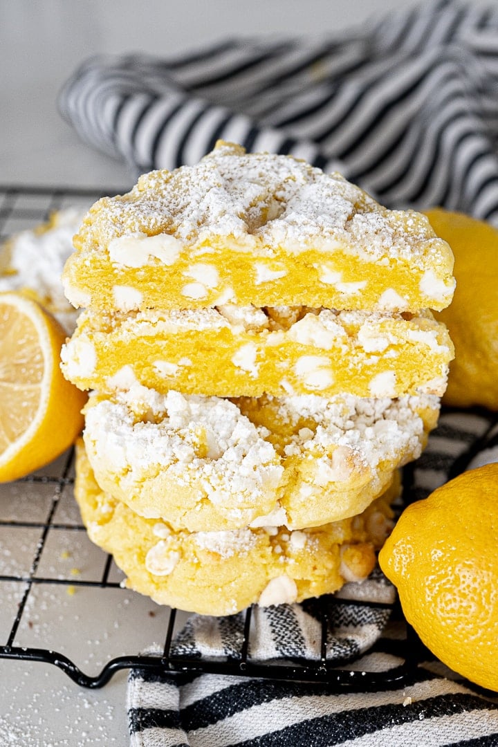 Lemon cookie cut in half, stacked on top of two other cookies on a cookie cooling rack.