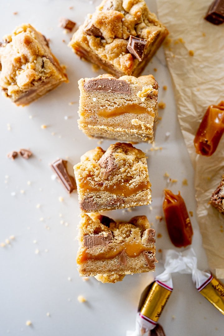caramel cookie bars with chocolate chips laying on the counter next to some caramels