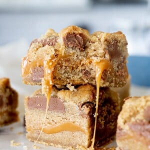 caramel cookie bars with chocolate chips stacked on top of each other. the top bar has a bite taken out of it.
