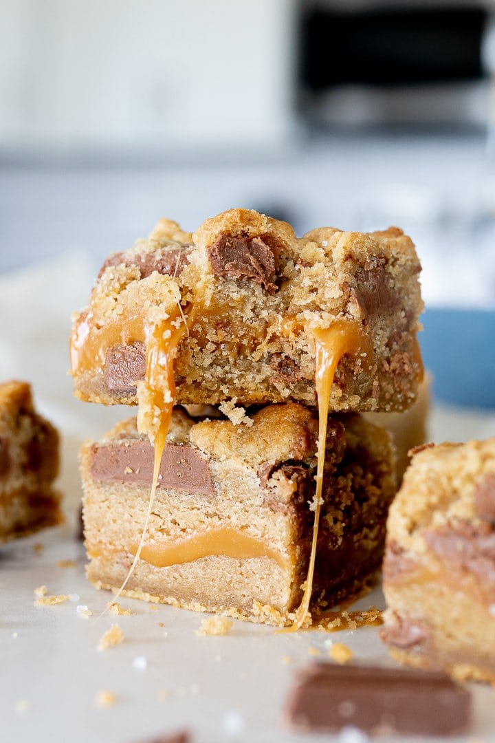 caramel cookie bars with chocolate chips stacked on top of each other. the top bar has a bite taken out of it.