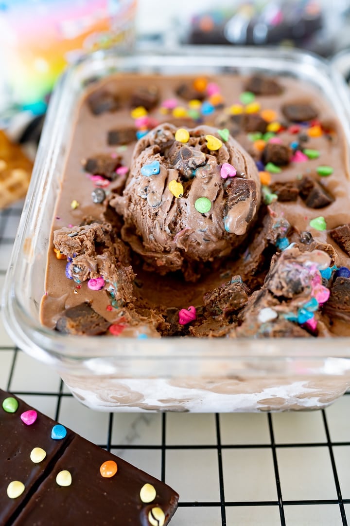 cosmic brownie ice cream in a glass container with a scoop of ice cream in the middle