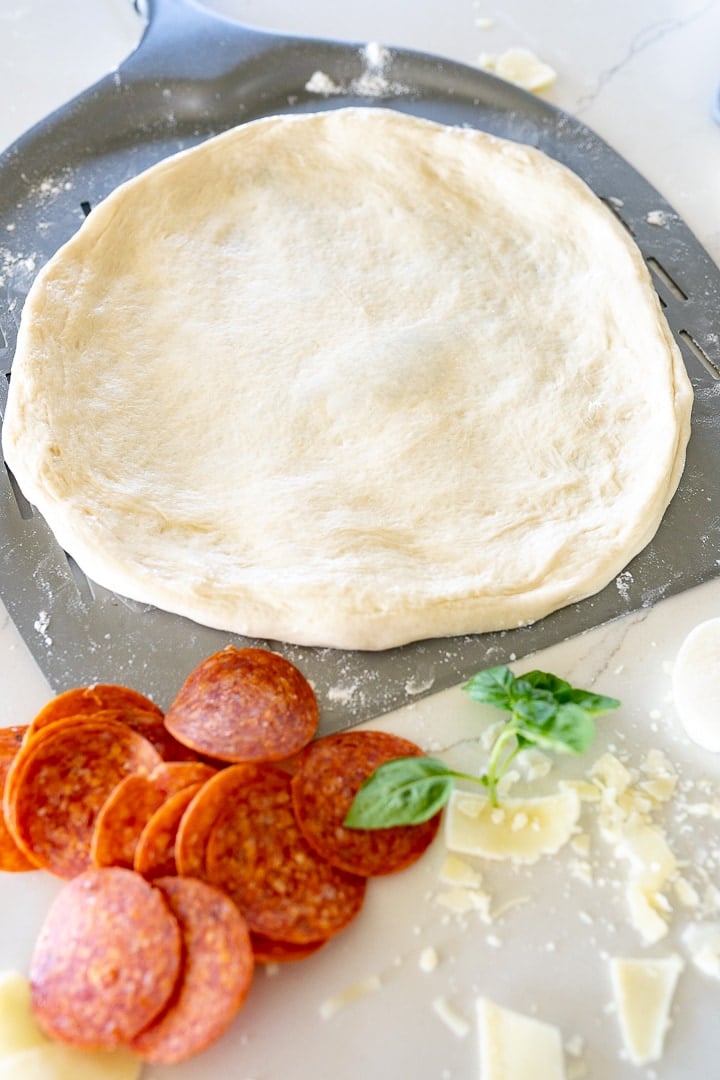 pizza dough on a pizza peel with pepperoni next to it. 