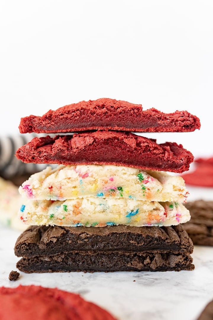 red velvet cookie cut in half stacked on top of a sprinkle cookie cut in half that is stacked on top of a chocolate cookie that was cut in half.