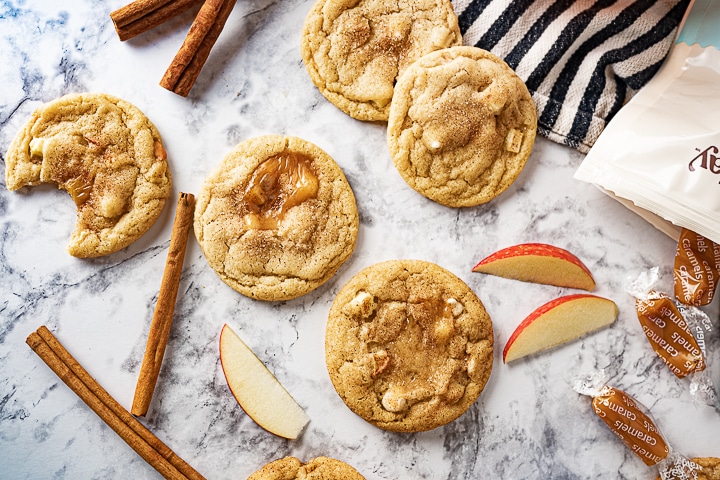 caramel apple cider cookies on the counter with apple slices and cinnamon sticks. 