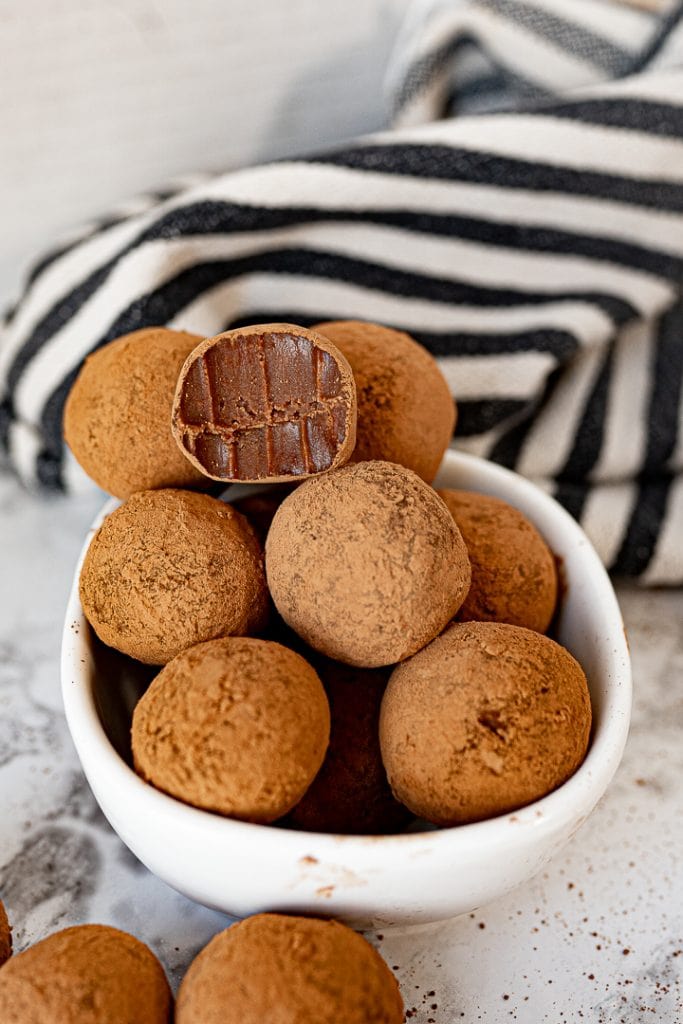 Chocolate truffles in a white bowl on the counter with a black and white striped towel in the background.