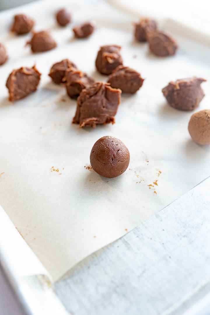 Chocolate truffles on a sheet of parchment paper with some rolled into spheres and others just portioned out on the sheet.