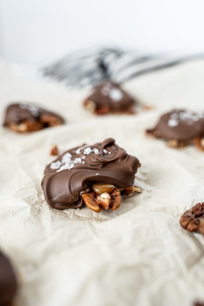 homemade chocolate turtles on parchment paper with sea salt on top.