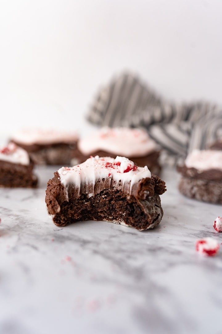 A peppermint chocolate crinkle cookie with bites taken out of it and more cookies in the background on the counter.