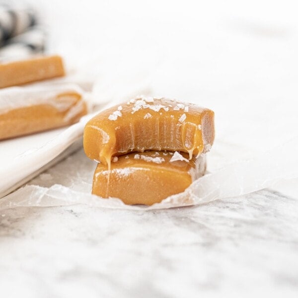 caramel squares on the counter stacked on top of each other. The top caramel has a bite taken out.