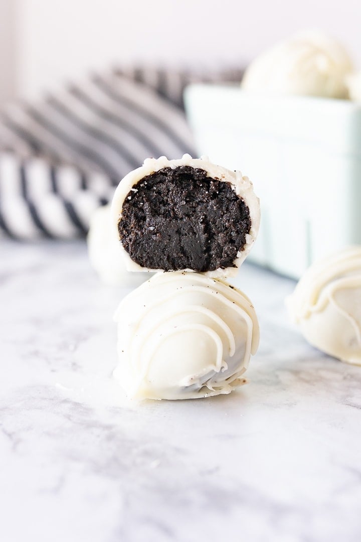 Two oreo truffles stacked on top of each other on the counter with a bite taken out of one truffle so you can see the oreo filling.