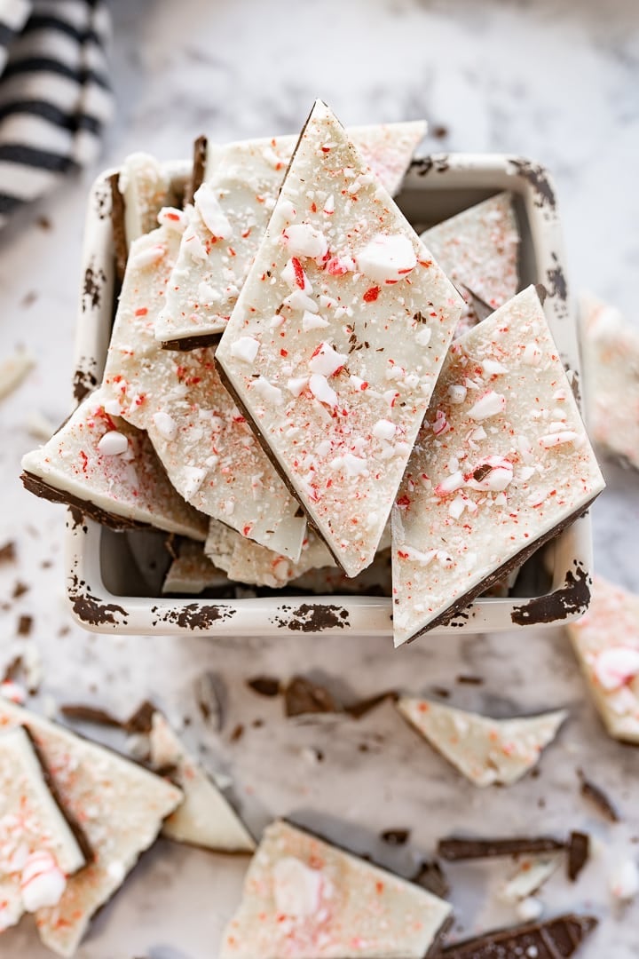 White chocolate peppermint bark sitting in a white dish with some pieces of the bark falling out onto the counter.