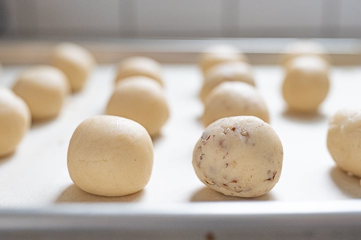 Balls of snowball cookie dough laying out on a cookie sheet, before they're covered in powdered sugar.